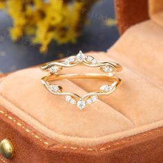 a gold ring with white stones in it sitting on a velvet box next to some flowers