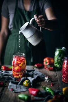 a person pours water into a jar filled with pickled peppers and bell peppers