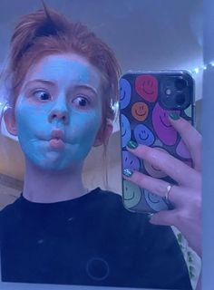 a woman taking a selfie in front of a mirror with her face painted blue