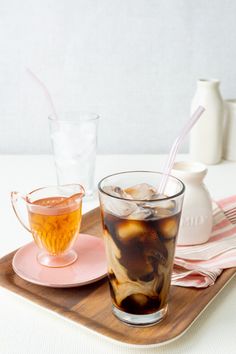 two glasses filled with liquid sitting on top of a wooden tray next to each other