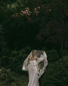 a woman in a wedding dress holding a veil over her head and looking at the camera