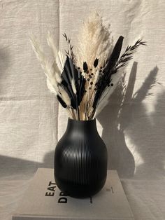 a black vase with white and black feathers in it on top of a table cloth