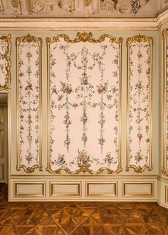 an ornate wallpapered room with gold trim and floral designs on the walls, along with wooden flooring