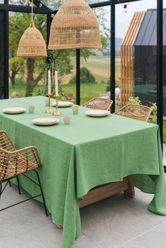 a green table cloth with wicker chairs and lamps on it in front of a glass wall