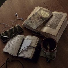 an open book sitting on top of a wooden table next to headphones and a cup