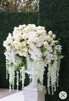 white flowers and greenery are arranged in an urn