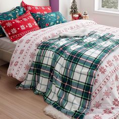 a bed covered in plaid and snowflakes next to a window