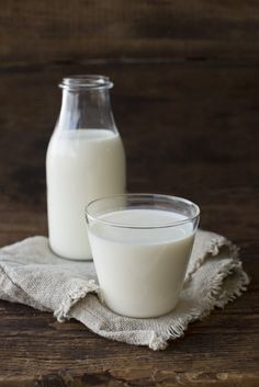 two bottles of milk sitting on top of a wooden table next to a glass filled with milk