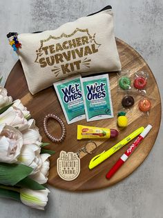 the teacher survival kit is laid out on a wooden platter with flowers and pens