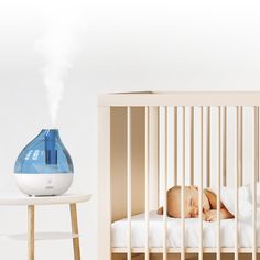 a baby sleeping in a crib next to an air humider on a table