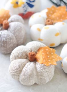 some white pumpkins are sitting on a table with yellow and orange leaves attached to them