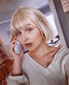 a woman talking on a cell phone while wearing a short blonde bobble haircut