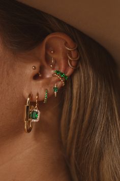 a close up of a person wearing ear rings and piercings with green stones on them