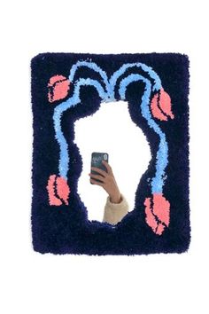 a hand holding a cell phone in front of a blue frame with pink flowers on it