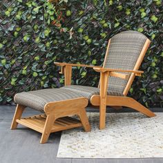 a chair and footstool sitting in front of a wall covered with green plants