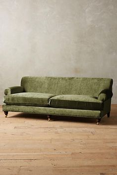 a green couch sitting on top of a hard wood floor next to a white wall