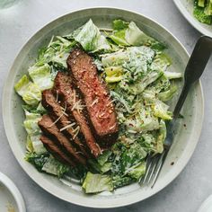 steak and lettuce in a white bowl with silverware next to it on a table