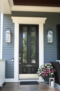 a black front door on a gray house with white trim and flowers in the pot