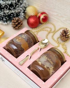 two chocolate covered jars with spoons in a pink box