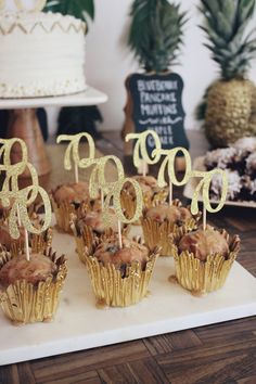 cupcakes with gold frosting are on a white platter next to pineapples