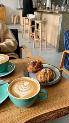 two cups of coffee and croissants are sitting on a table in a cafe