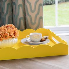 a yellow tray with a cup and saucer on it next to a vase filled with flowers