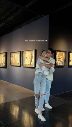 a man and woman hugging each other in front of pictures on the wall behind them