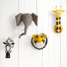 three animal head mounted to the side of a white wall next to two giraffes and an elephant