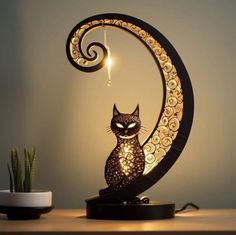 a cat sitting on top of a table next to a lamp that is shaped like the moon