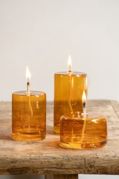 two yellow glass candles sitting on top of a wooden table next to eachother