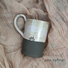 a coffee cup with a bicycle on it sitting on top of a bed covered in fabric