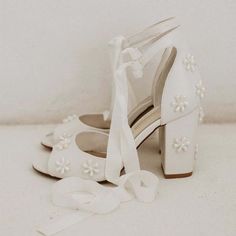 a pair of white shoes with flowers on the heel and a ribbon tied around them