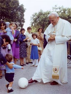 a little boy playing with a soccer ball in front of a pope and some people