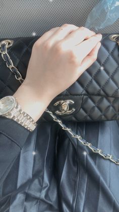 a woman's hand holding onto a black purse with chains on the wrist and chain around it