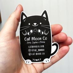 a person holding up a black and white business card with a cat moon logo on it