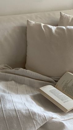 an open book sitting on top of a bed next to two pillows and a pillow case