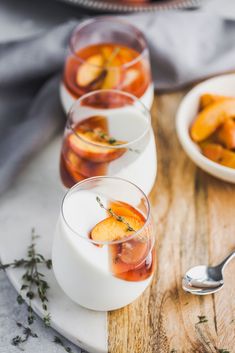 three glasses filled with drinks sitting on top of a wooden table next to silverware