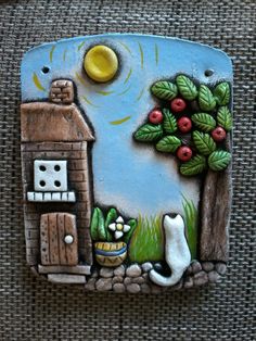 a ceramic tile with a house and cat in the grass next to a small tree