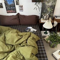 an unmade bed in a room with pictures on the wall above it and plants