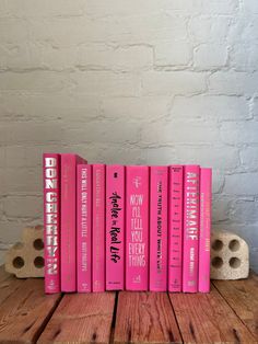 a stack of pink books sitting on top of a wooden table next to a brick wall