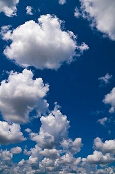 an airplane is flying in the blue sky with white clouds and some grass on the ground