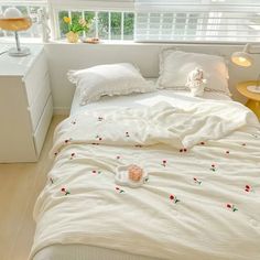 a bed with white linens and red flowers on it in front of a window