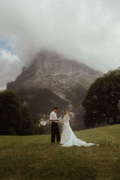 a bride and groom standing in front of a mountain with mist coming from the top