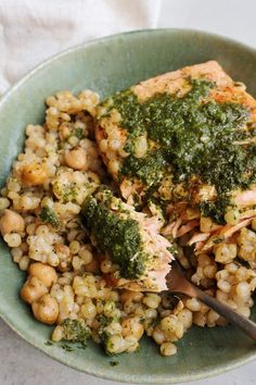 a green bowl filled with meat and vegetables on top of a white table cloth next to a fork