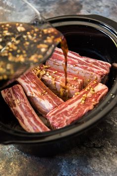 someone is pouring sauce on raw meat in a slow cooker with other food items