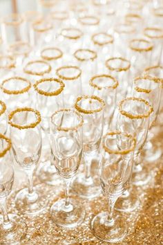 champagne glasses lined up on a table with gold sequins and glitter around them