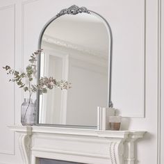 a white fireplace with a mirror and vase on it