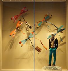 a display case with an assortment of kites on it's glass walls, including a mannequin