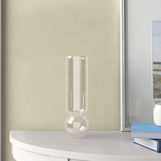 a white shelf with a glass vase on top of it next to a blue book