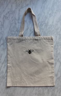 a canvas bag with a bee embroidered on the front and side, sitting on a marble surface